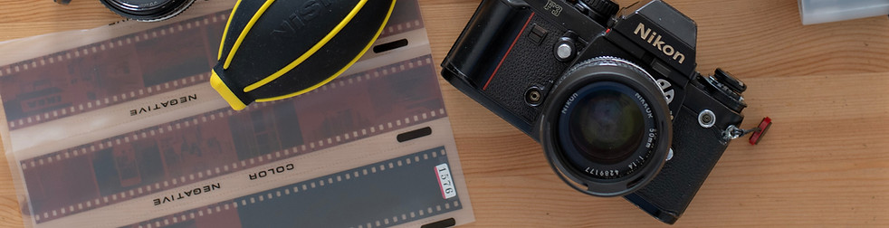 Film rolls, Nikon camera, lens, and accessories on wooden table theshutterbug.