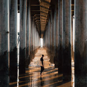 Person walking under a pier with a surfboard, theshutterbug, sunny day.