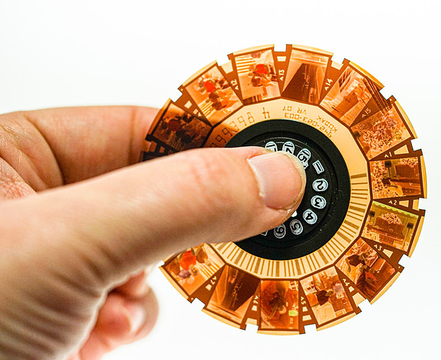 Hand holding a film reel with visible photos, theshutterbug for a close-up shot.
