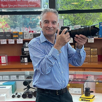 Man holding camera in camera store, "Get Your Passport Photos Here" theshutterbug staff Mazda